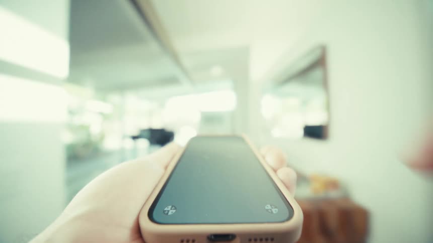 A close view shows a hand holding a smartphone with tracking markers on the screen while walking through a modern house with large windows and wooden doors