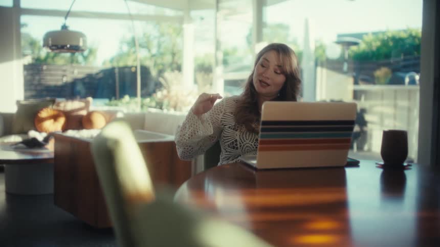 Woman seated at a table uses a laptop in a bright room