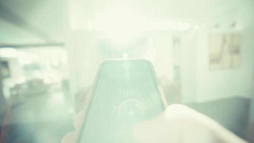 Person scrolling on a smartphone walks through a sunny building