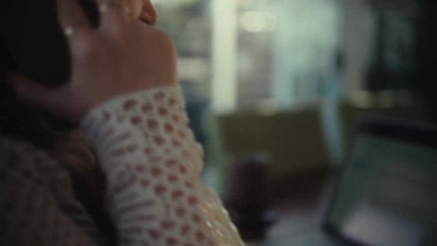 The woman is looking at her laptop while talking on her cell phone