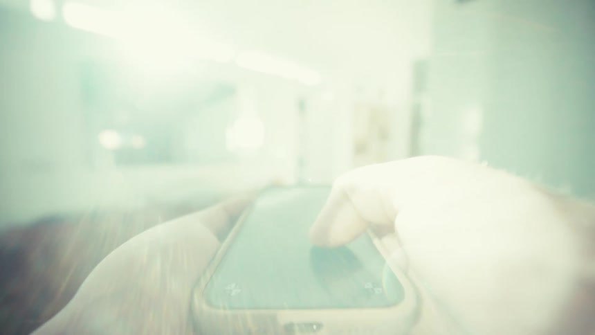 Hands hold a smartphone with the screen off in a blurred indoor setting