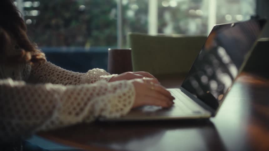 Young woman sits at a table typing on a laptop computer