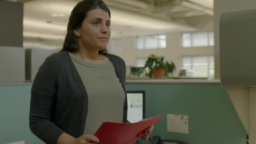 Woman looking at a folder and then to her watch in an office
