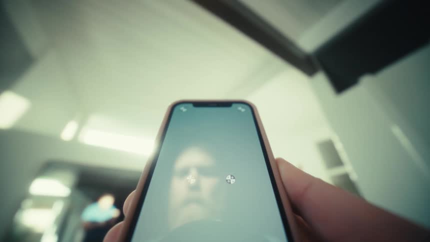 Man holds a smart phone in his hand and his reflection is seen on the screen