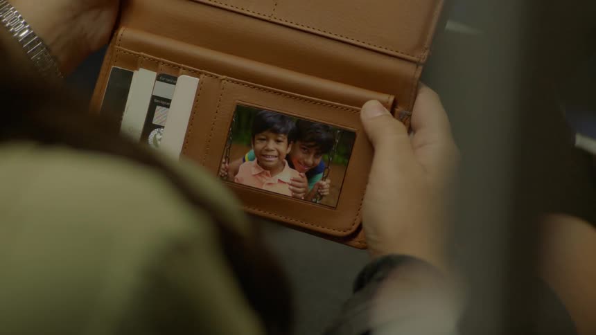A woman is opening a wallet and looking at the photo inside