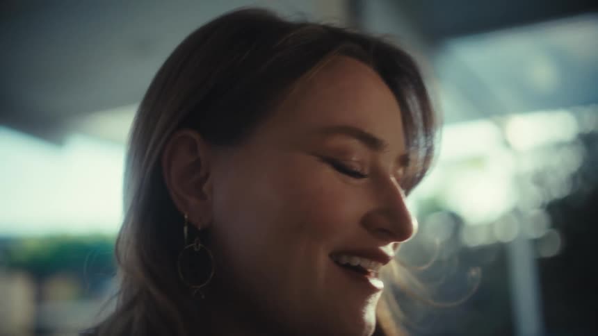 A woman in close up smiles gently with her eyes closed in a moment of quiet happiness indoors