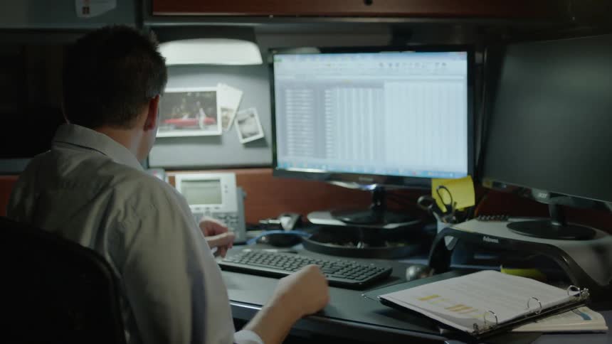 A man working at a computer pulls a photograph from his cubicle wall
