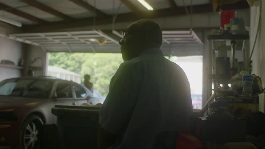 A man standing in a garage nods and talks to someone