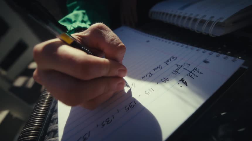Woman sitting on a deck near a staircase makes notes while studying outdoors on an autumn day