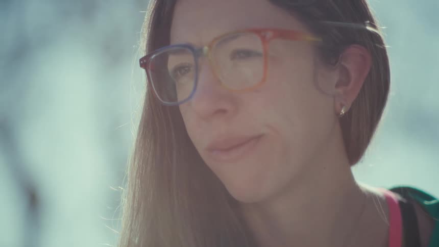 Young adult woman wearing glasses writing on a notebook with a contemplative facial expression outdoors during day time