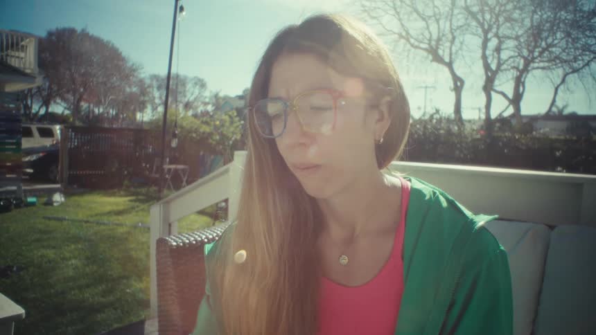Teenage girl sitting outside typing on a laptop computer as she pauses and holds her pen