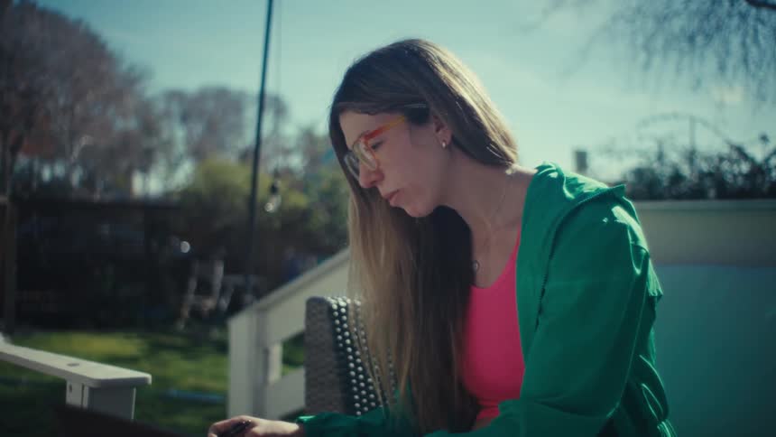 A woman is sitting outside typing on a laptop as she sits on a couch