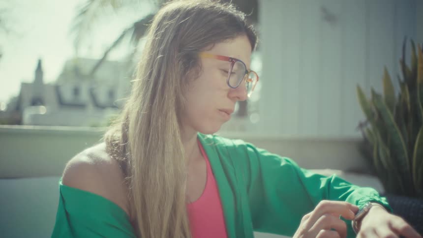 Teenage girl sitting outside typing on a laptop computer as she stops to look at her wristwatch then continues to type