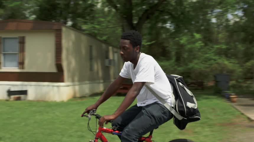 Man wearing a backpack riding a bike in a trailer park