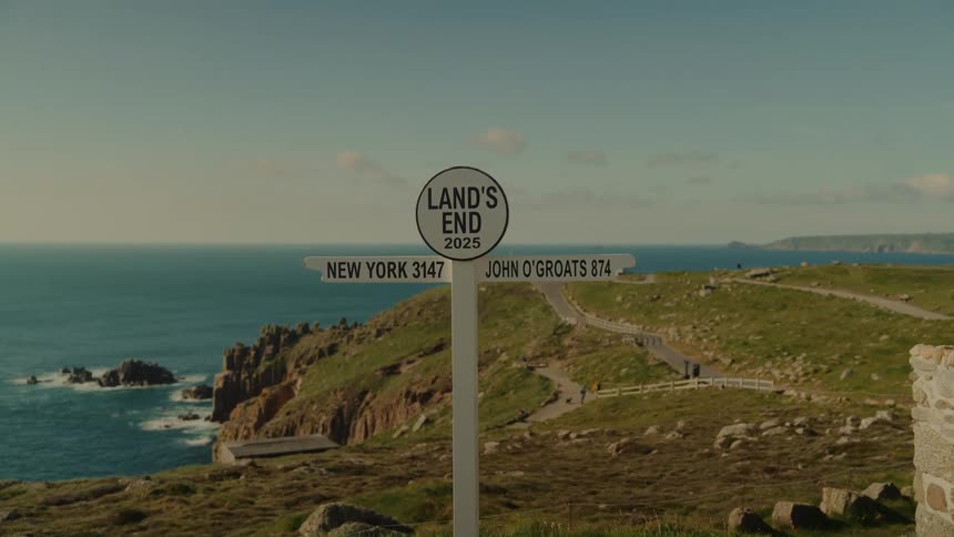 Road sign labeled lands end stands in a coastal area while people stand in the road in the background