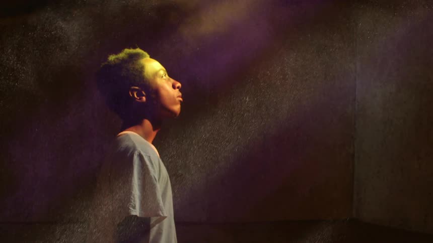 A boy looks up while dust particles glimmering in the light fall down around him