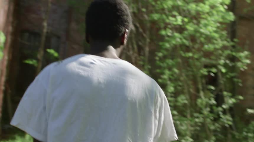 Man walking through trees near abandoned brick building
