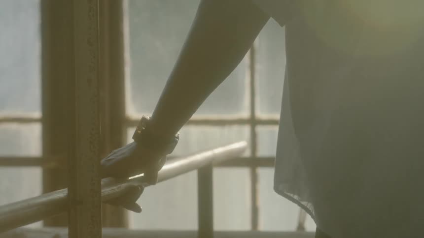 A man rests his hand on a rail as sunlight shines in the window