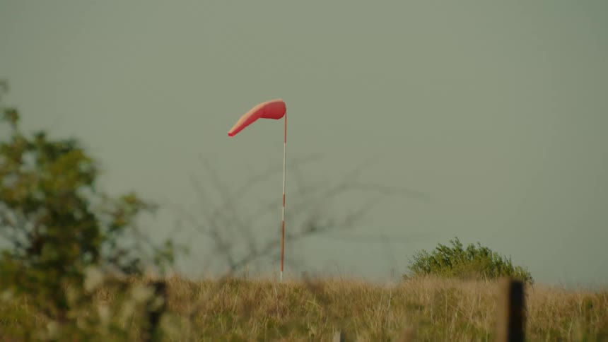 Red windsock mounted on a grassy hill beneath a clear sky