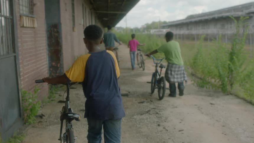 Children are walking their bicycles past a building
