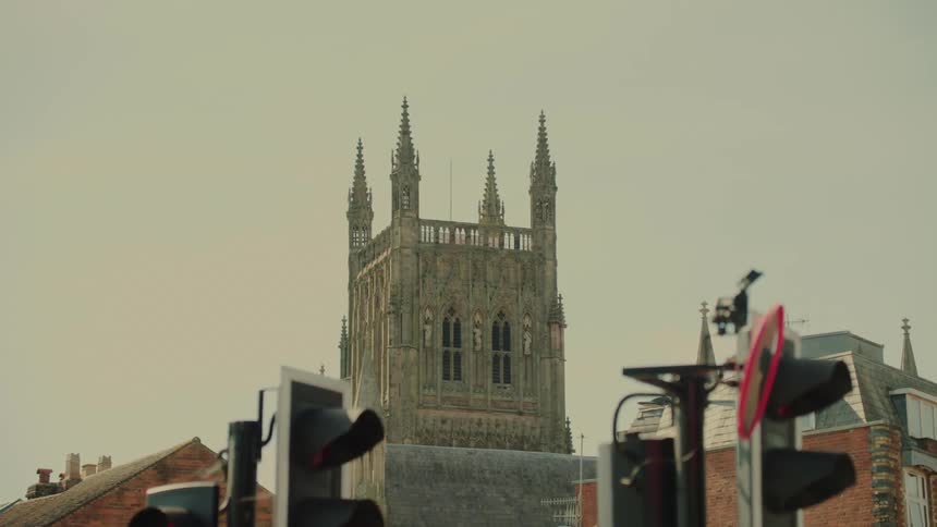 A couple of streetlights at an intersection as the lights change with a castle tower in the background on a cloudy day