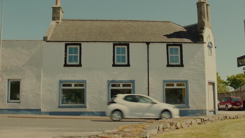 A car moving in front of a whitepainted building at daytime
