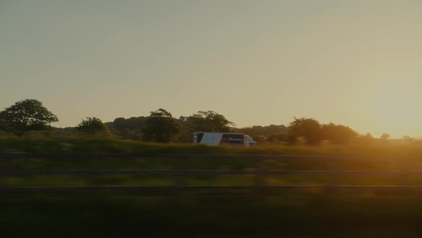 Commercial trucks drive along a country road near sunset during the summer