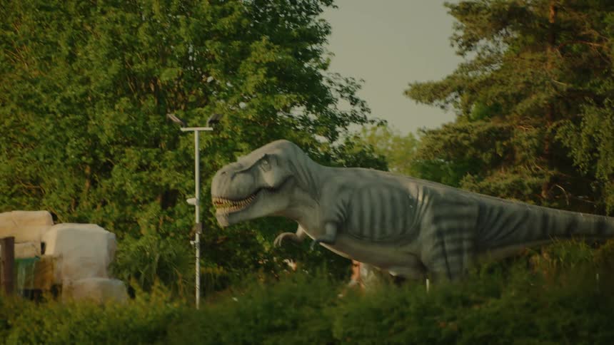 A realistic dinosaur display stands tall surrounded by trees and bushes in an outdoor setting