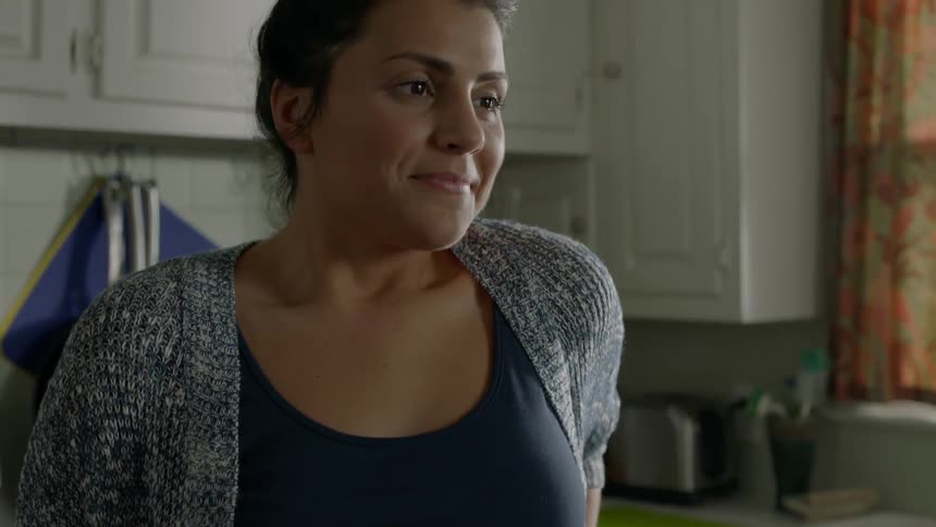 A woman looks at her phone and smiles while standing in a kitchen