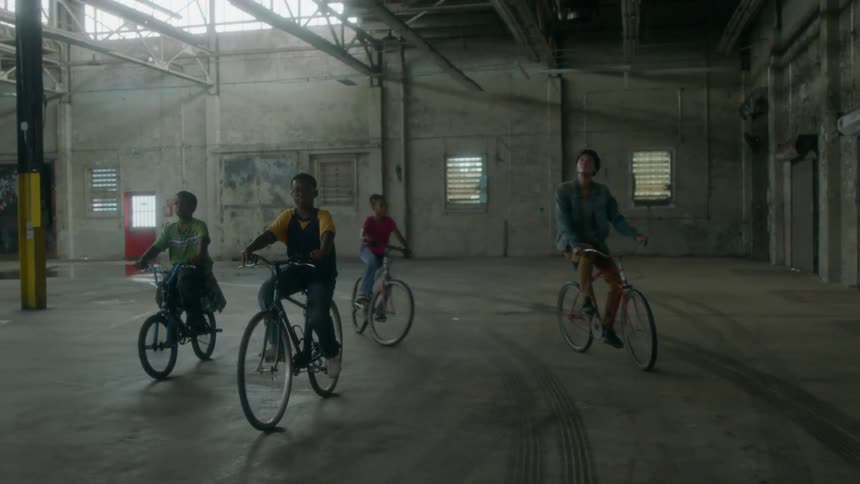 Three children ride bikes in an abandoned warehouse