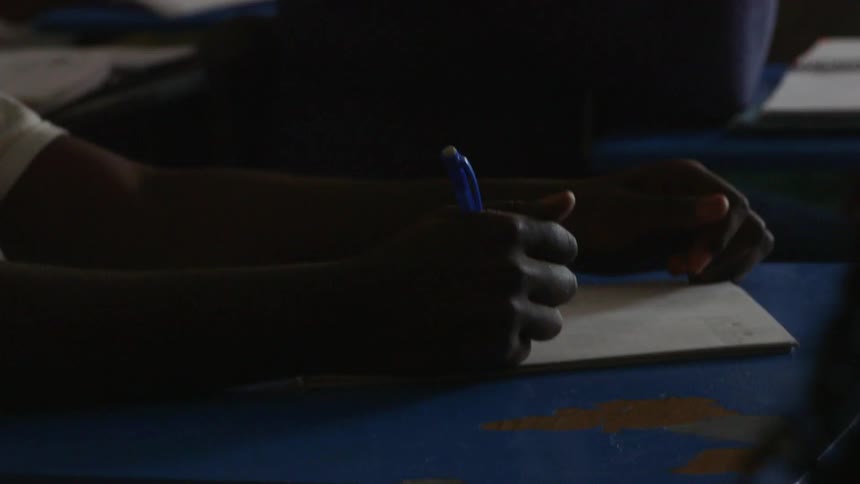 Person writing on a yellow tablet in a classroom setting