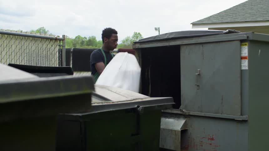 A man throws bags into a dumpsters