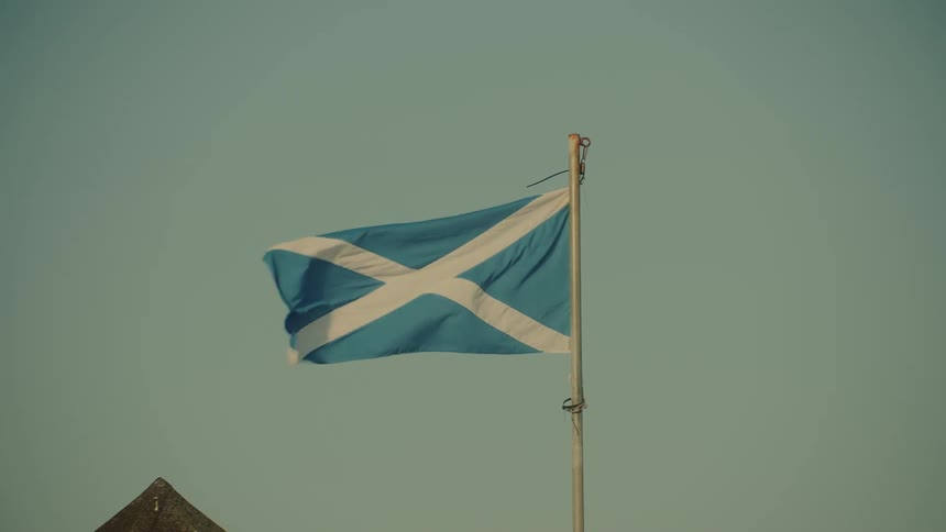 Blue and white colored flag flaps in the wind against a light blue sky