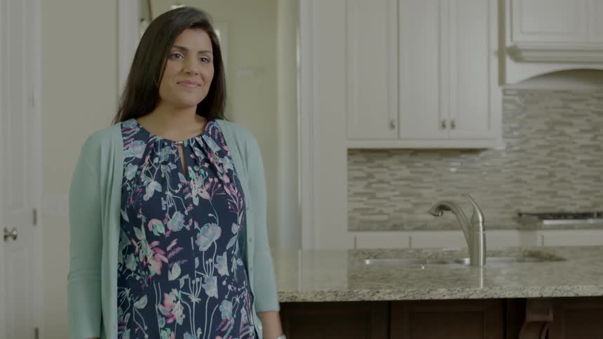 A woman smiles as two kids run through the kitchen