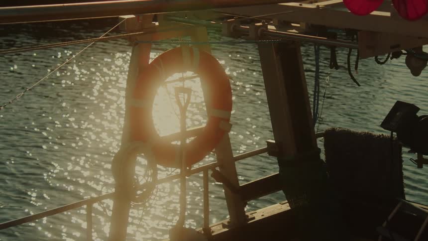Life preserver hanging on a boat that is rocking in the waves of sparkling water