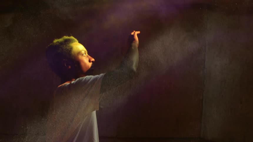 Man raising his hand to block something as beams of light show the dust in the air