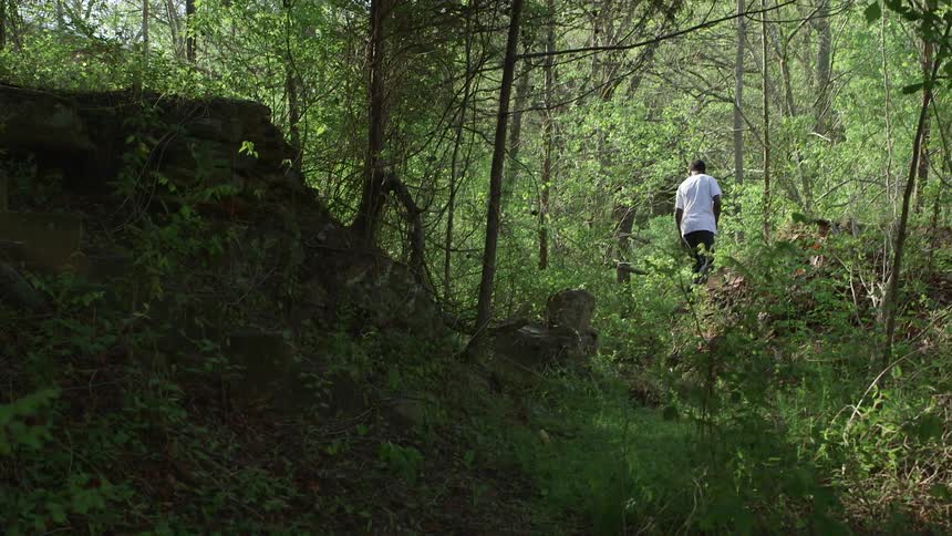 A man in a white shirt hikes through the woods