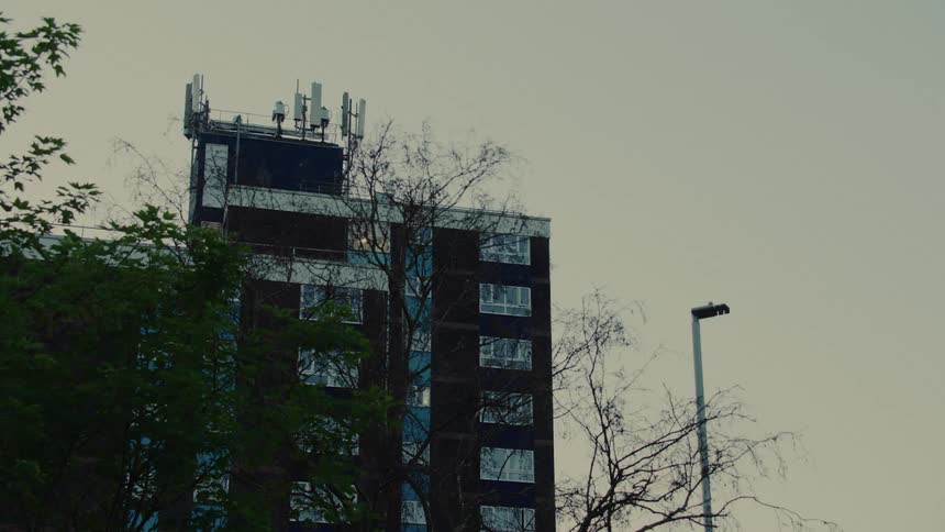 Urban building with antennas on the roof among trees and streetlights