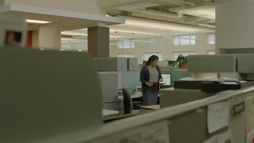 A woman picks up a pink folder and walks away from her desk