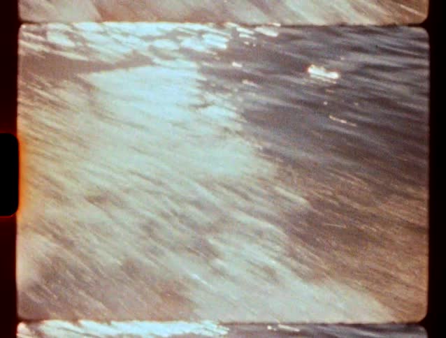 A closeup of water rushing by captured in a grainy vintage film style with visible sprocket holes on the side the sunlight reflects off the moving surface creating bright highlights across the churning waves