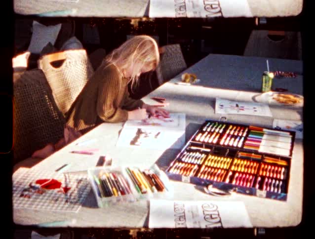 A blonde girl colors a picture while sitting at a long table