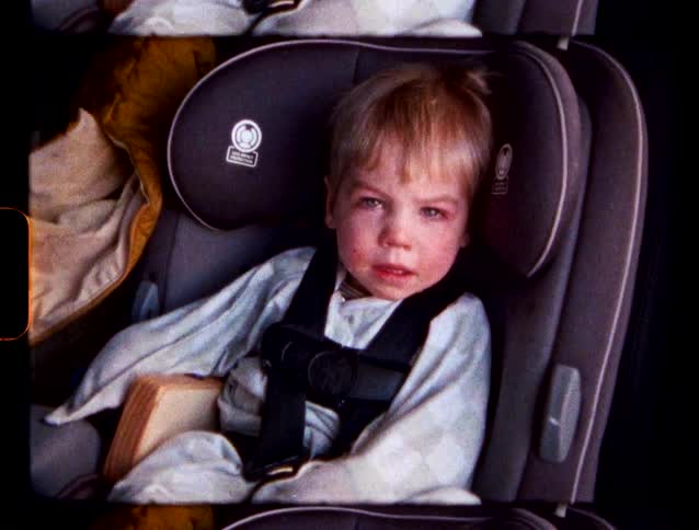 Blonde baby boy sitting on a child safety seat on a vehicle indoors during day time