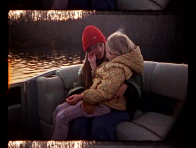 A woman in a red beanie holds a child in a boat tenderly caressing their face at dusk