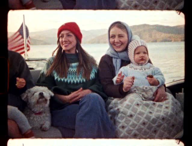 A group of people riding on a boat with a dog an American Flag blows in the wind behind them