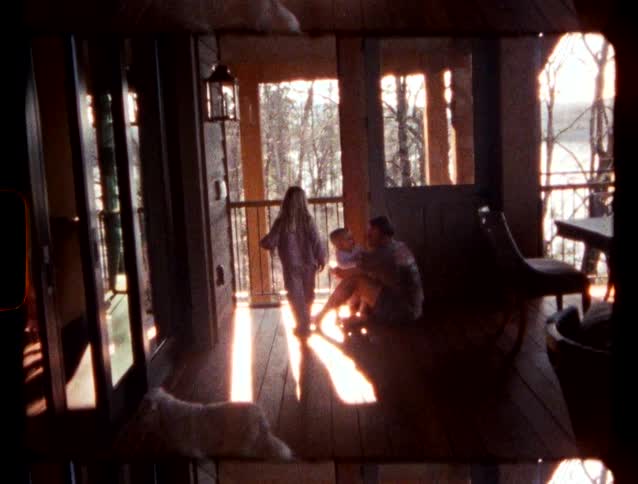 A father and his son sit on a sunlit wooden porch while a girl walks toward them