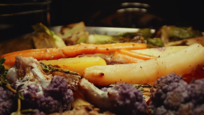 Tray with purple cauliflower carrots and other vegetables roasting in the oven