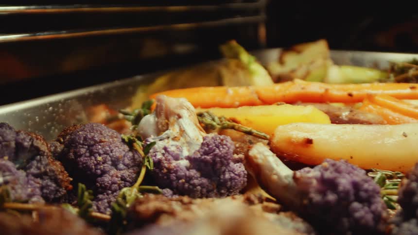 Various vegetables lie on a roasting sheet in the oven