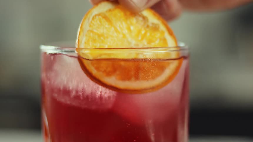 A man puts a slice of orange in a glass of juice before picking it up