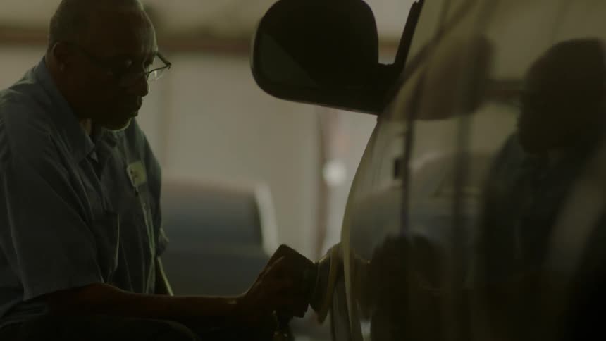 A man buffs the front fender of a car in a garage