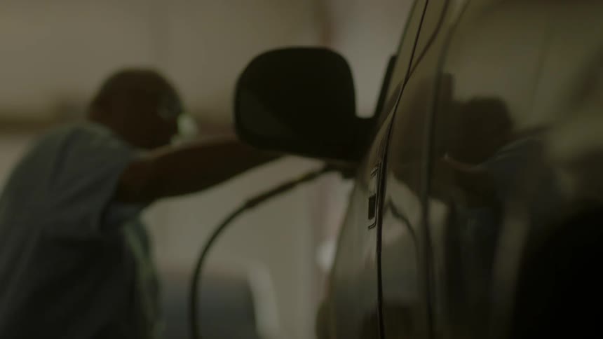 A man rubs a buffer over the hood of a car
